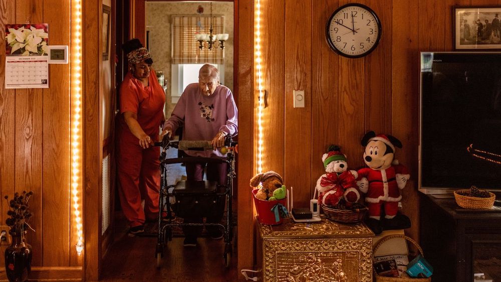 Savanna Hollar, 90, navigates a hallway as home health aide Tangie Enoch looks on.